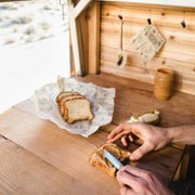 Man's hands spreading bread butter on sliced bread as other sliced brad is wrapped in  an reusable Abeego wrap.