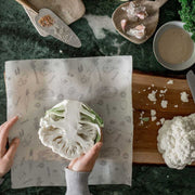 Woman's hands laying a half cut cauliflower on a large Abeego wax wrap.