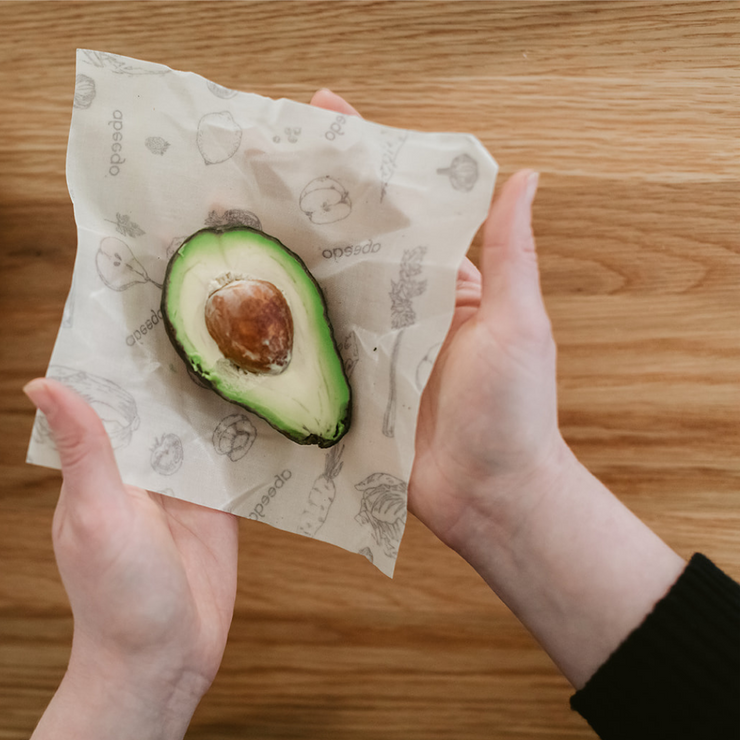 A pair of hands about to wrap half an avocado with a small Abeego beeswax wrap.