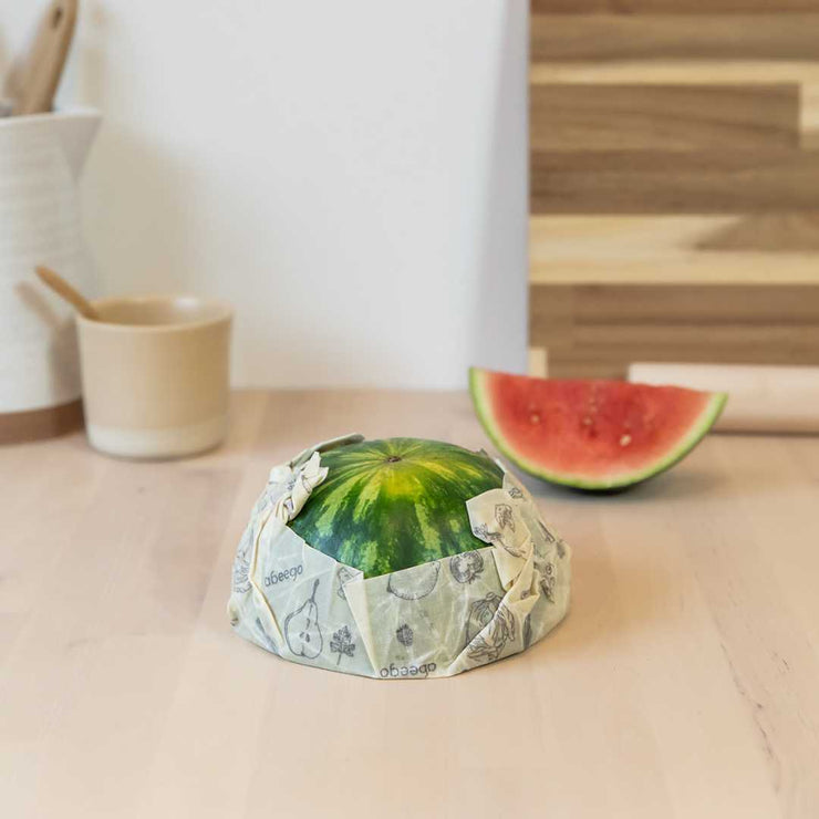 A half cut watermelon covered by a large Abeego food wrap.