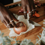 A pair of hands unwrapping  a small Abeego food wrap, covering half an onion.