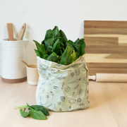 Abeego large rectangle beeswax food wrap folded into a bag and filled with fresh spinach.