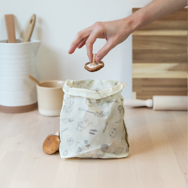 A hand is dropping a mushroom into a medium rectangle Abeego beeswax wrap folded into a bag.
