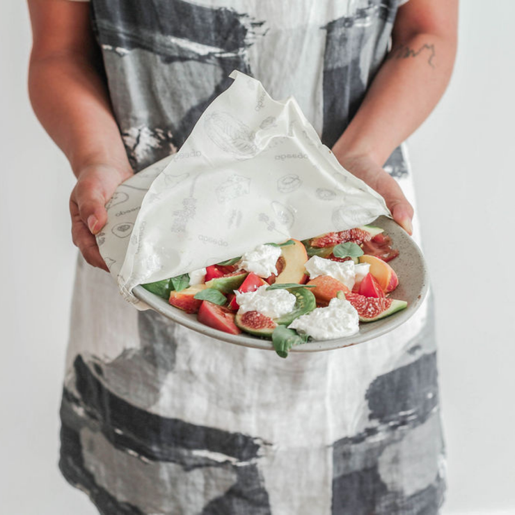 A woman holding a fresh summer salad dish, partially covered by an Abeego wax wrap.
