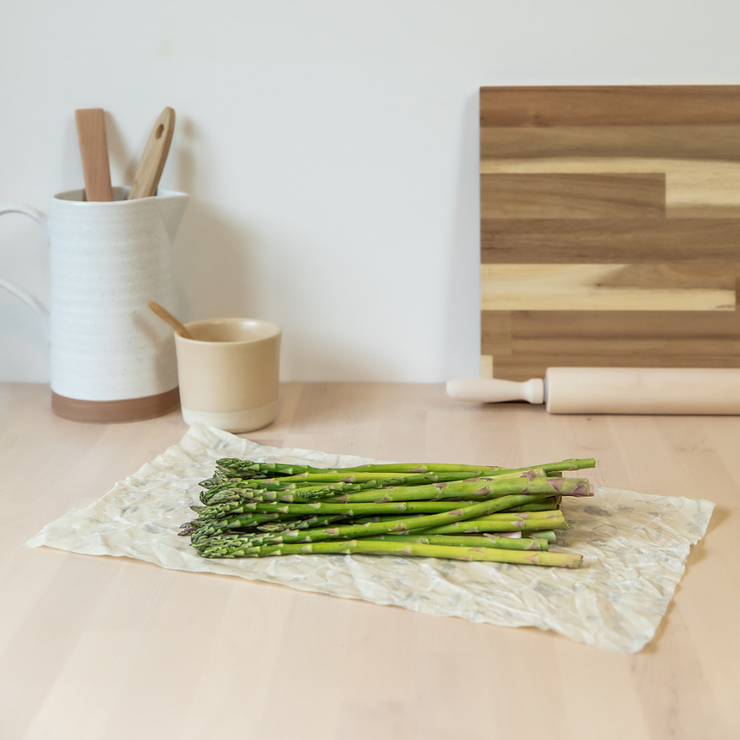 A bunch of asparagus laying on an Abeego medium rectangle beeswax wrap. 